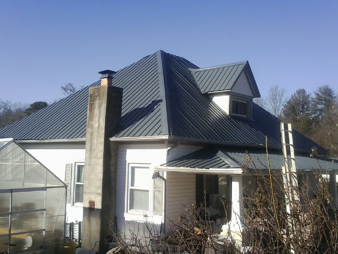 Dark blue standing seam metal roof on a white farmhouse with dormer — Slate & Tile Roof Repair by Roofing Brothers in Dodge Center