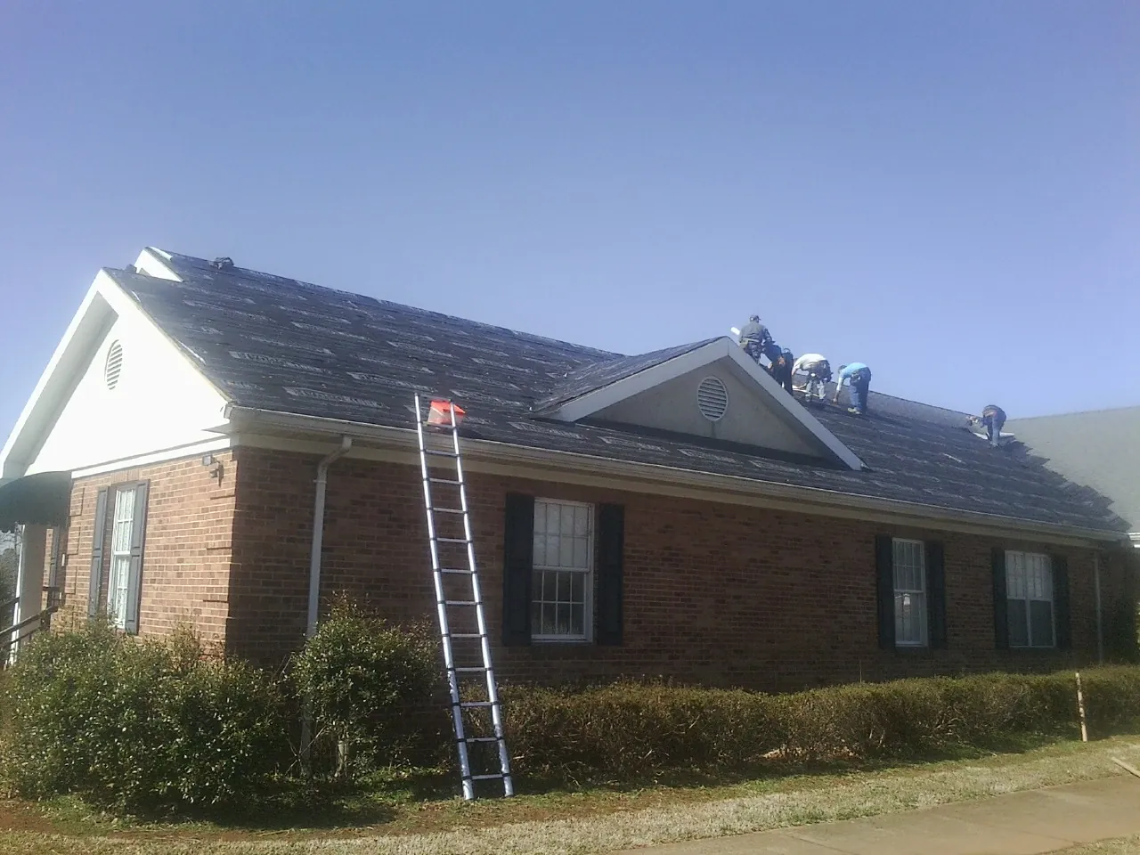 Crew tearing shingles off a brick ranch roof with a ladder set — Metal Roof Repair work by our crew in Dodge Center