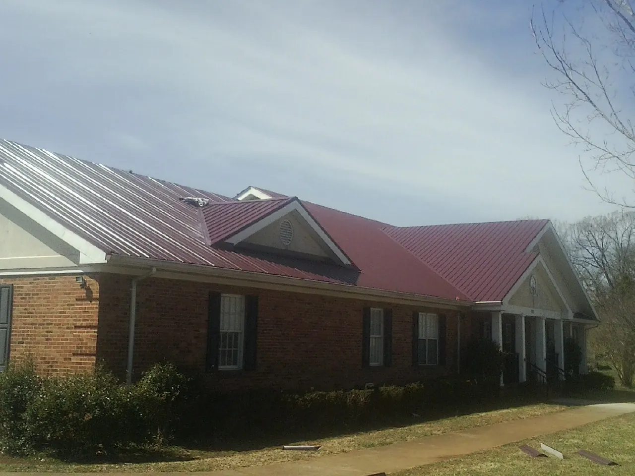 Red metal roof with gabled entries on a long brick building, from a Hail Damage Roof Repair job in Dodge Center