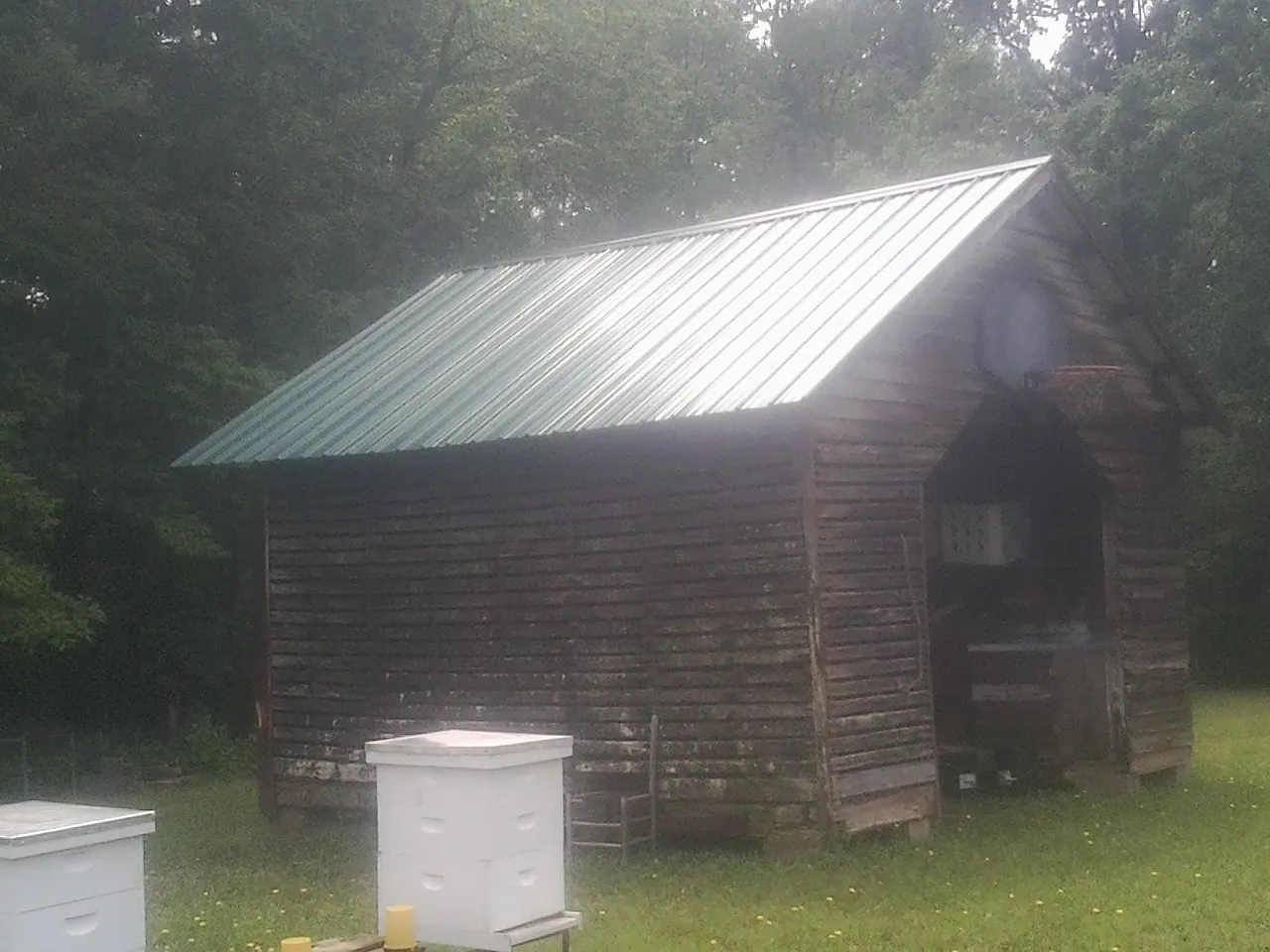 Green metal roof on a weathered barn beside stacked beehives in Dodge Center