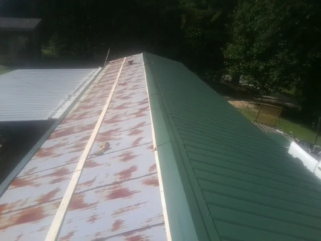 Old rusted panels beside newly installed green metal roofing — Wind Damage Roof Repair by Roofing Brothers in Dodge Center