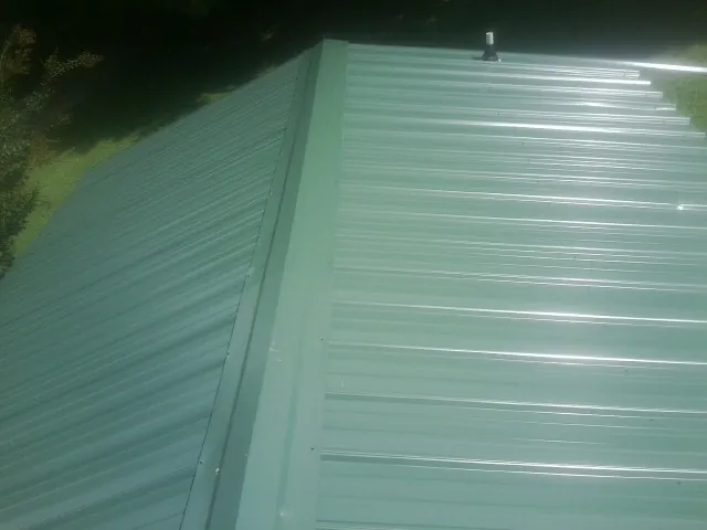 New green metal panels meeting at the ridge of a roof — Flat Roof Repair work by our crew in Dodge Center