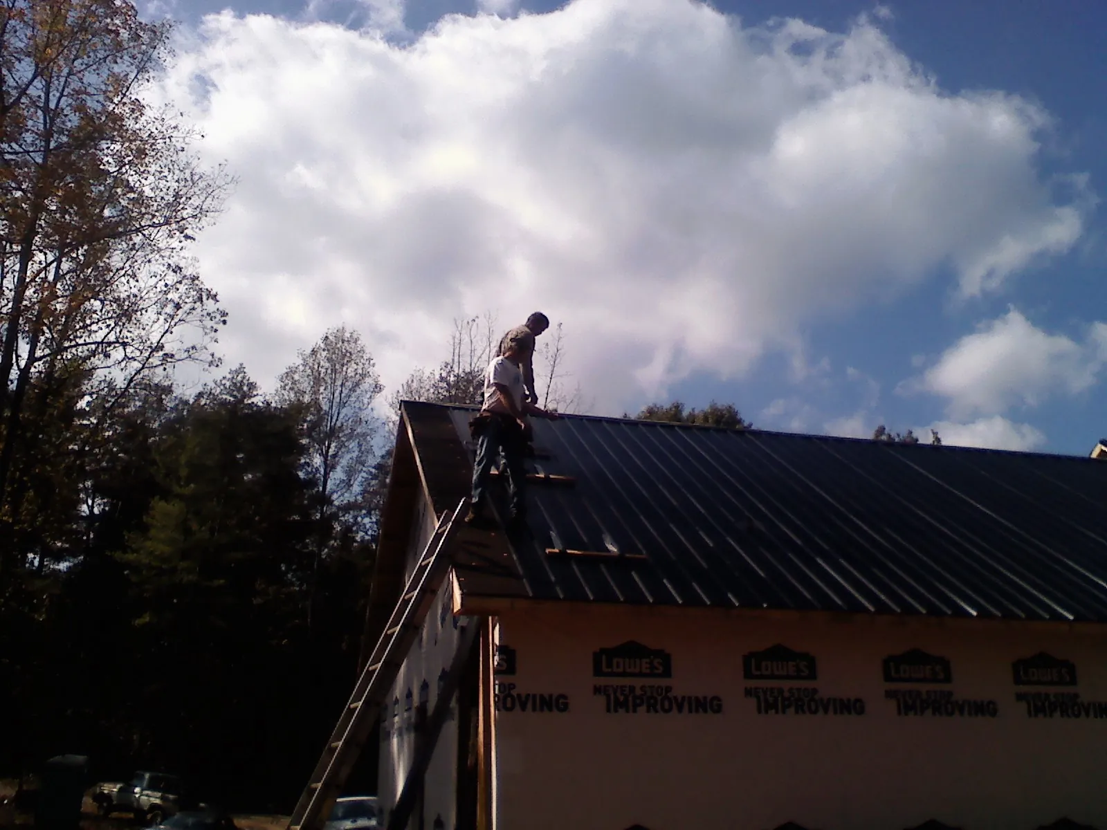 Roofer fastening dark metal panels high against a cloudy sky, from a Roof Inspection job in Dodge Center