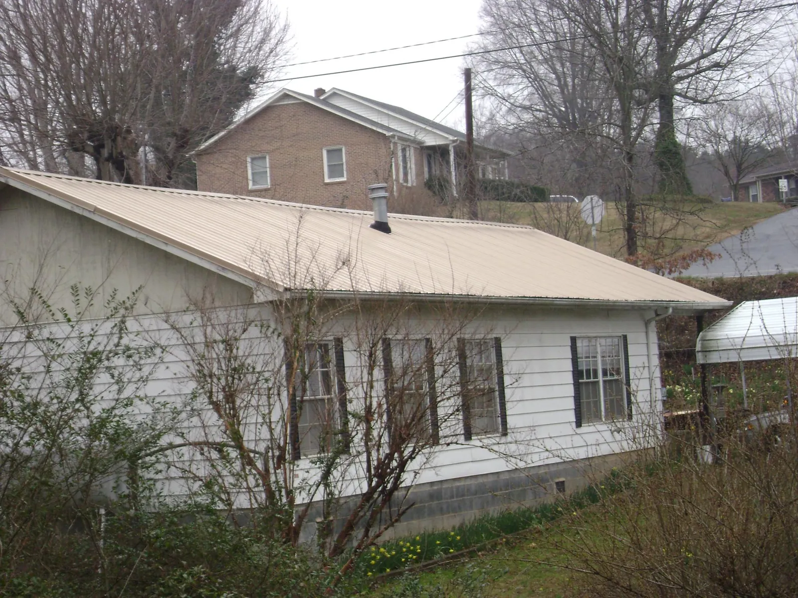 Tan metal roof on a white sided house set into a hillside — Commercial Roofing by Roofing Brothers in Dodge Center