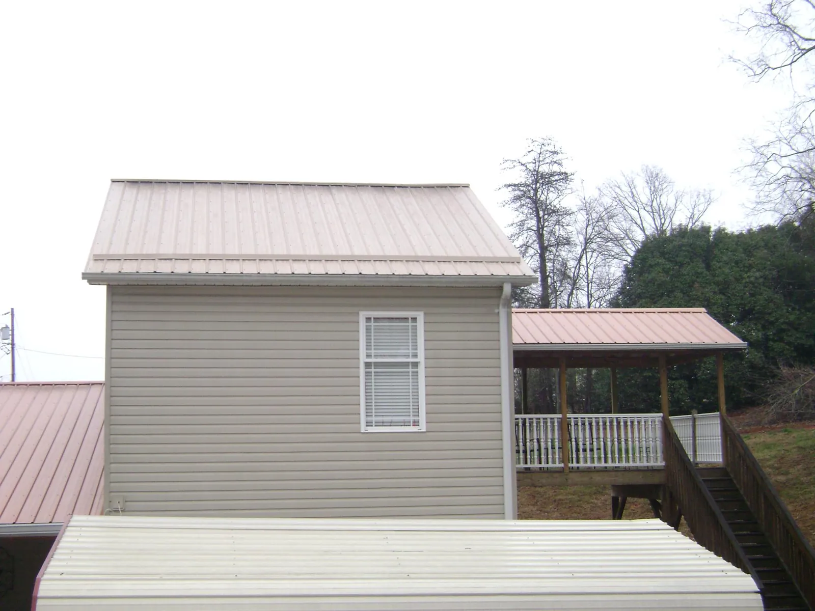 Tan metal roofs on a two story addition and attached porch, from a Roof Replacement job in Dodge Center